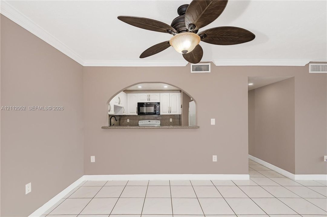 Ceramic tile flooring, arched wall pass-through, ceiling fan with integrated lighting, and white cabinetry