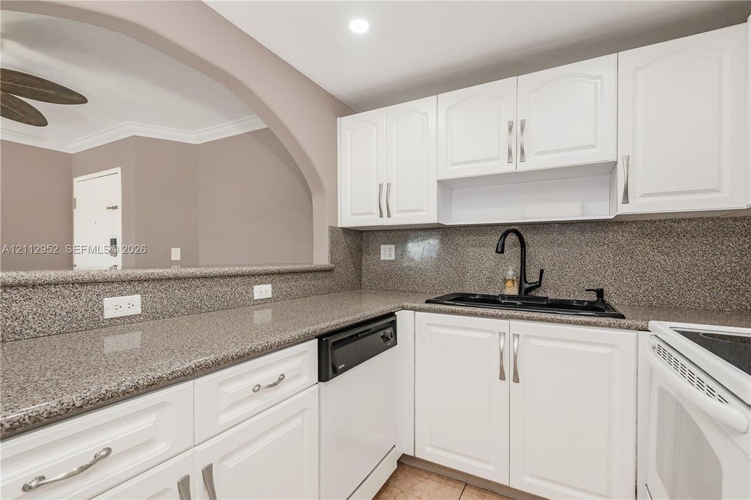 Kitchen featuring white shaker-style cabinetry, speckled stone countertops, a matte black dual-handle faucet, integrated black sink, and a decorative arched pass-through opening