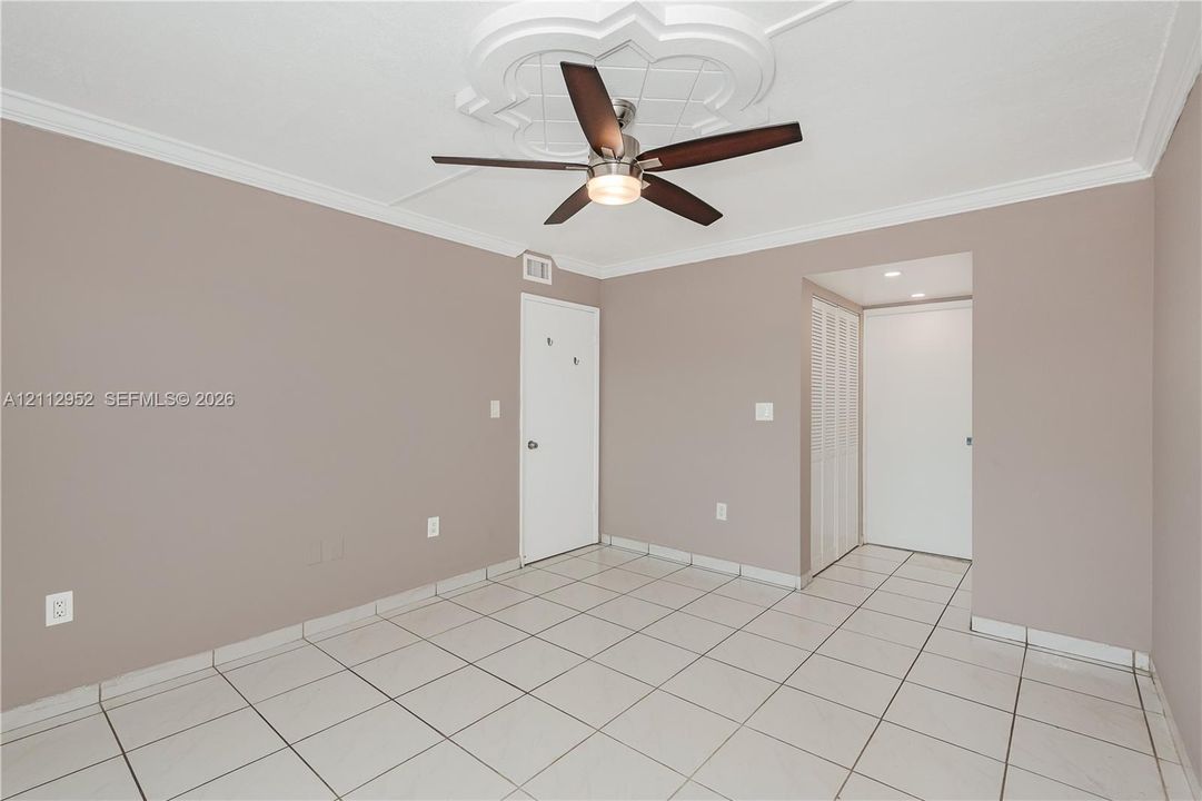 Interior room featuring large-format ceramic tile flooring, a decorative ceiling medallion, a multi-blade ceiling fan with integrated light fixture, and crown molding