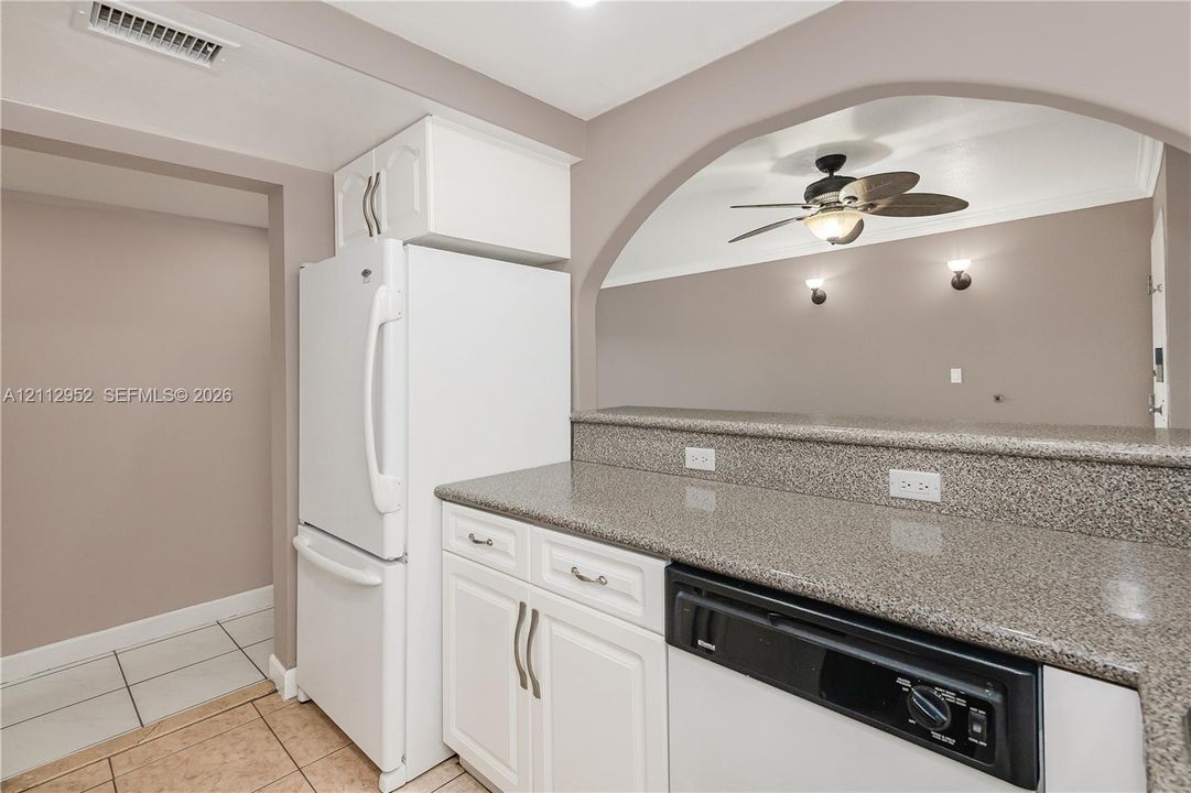 Kitchen featuring speckled stone countertops, white cabinetry with silver-tone hardware, a white refrigerator, a black dishwasher, and an arched wall opening