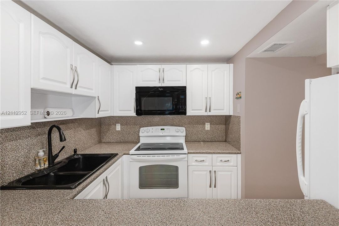 Kitchen featuring white cabinetry with silver-tone hardware, stone-finish countertops, black double-basin sink with a matte black high-arch faucet, and white appliances including a range and over-the-range microwave