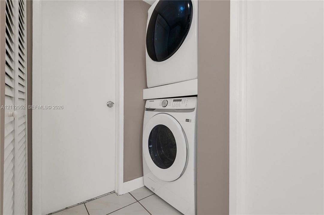 Stacked laundry unit featuring a high-capacity front-load washer and matching dryer, louvered closet doors, and ceramic tile flooring