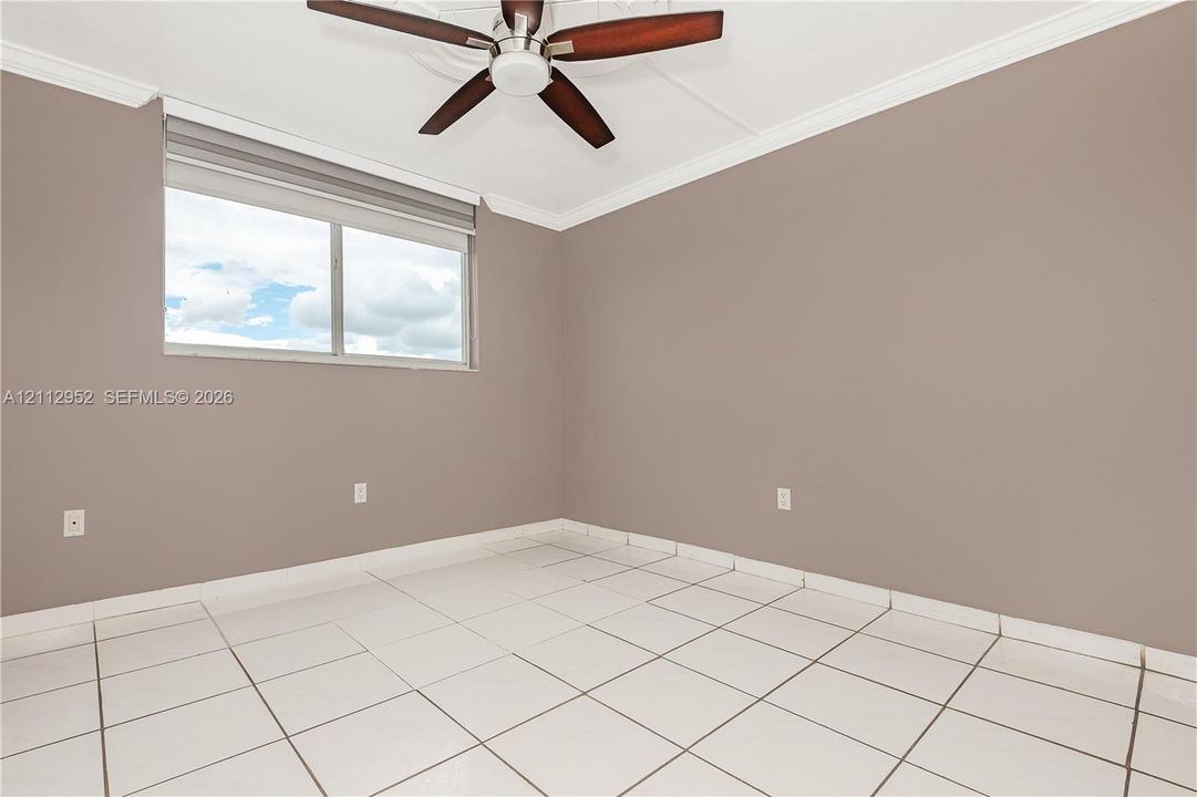 Neutral-toned walls featuring crown molding, ceramic tile flooring, a dual-pane window, and a ceiling fan with integrated lighting