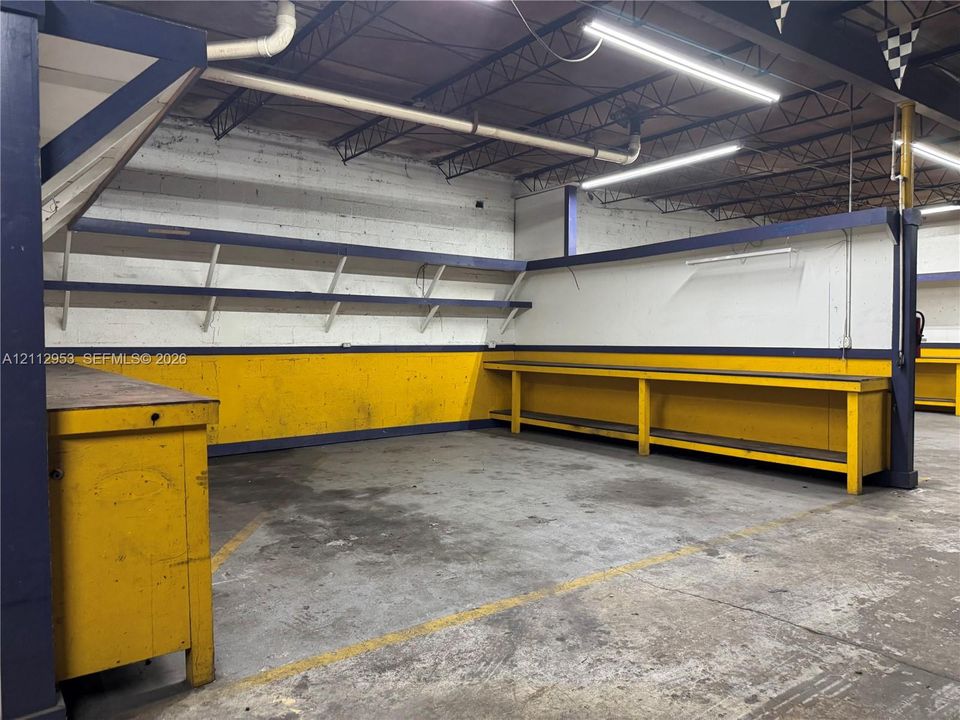Industrial space featuring exposed ceiling trusses, concrete flooring, dual-level built-in workbenches, and linear LED lighting