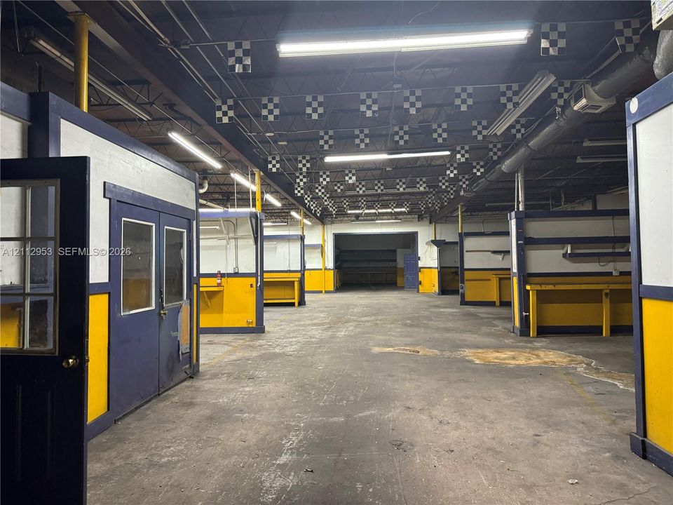 Expansive industrial interior featuring a concrete floor, exposed ceiling structure with linear lighting, and multiple built-in partitioned work stations