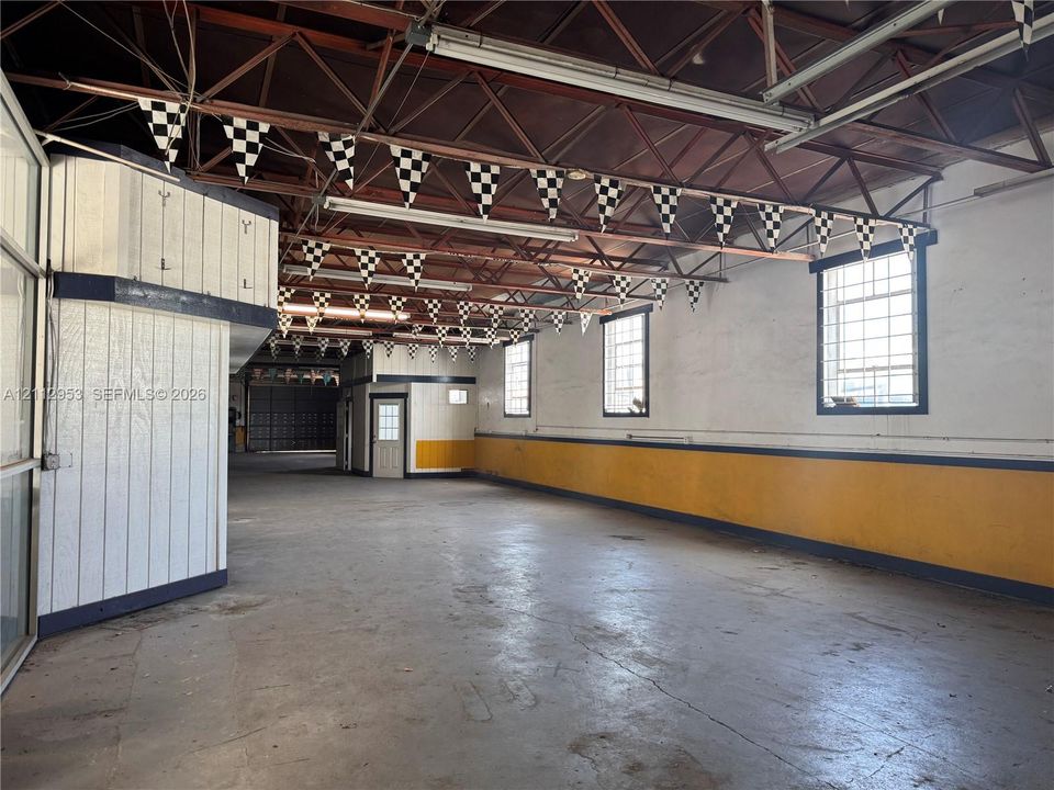 Expansive industrial-style interior featuring high-vaulted exposed steel truss ceilings, concrete flooring, multi-pane windows, and a built-in partition wall