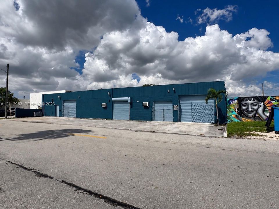 Commercial exterior featuring blue corrugated metal siding, four metal roll-up bay doors, and external wall-mounted HVAC units