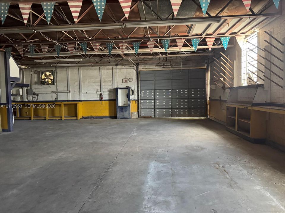 Expansive industrial workshop featuring a concrete floor, high vaulted exposed-truss ceiling, large sliding metal door, and built-in work counters