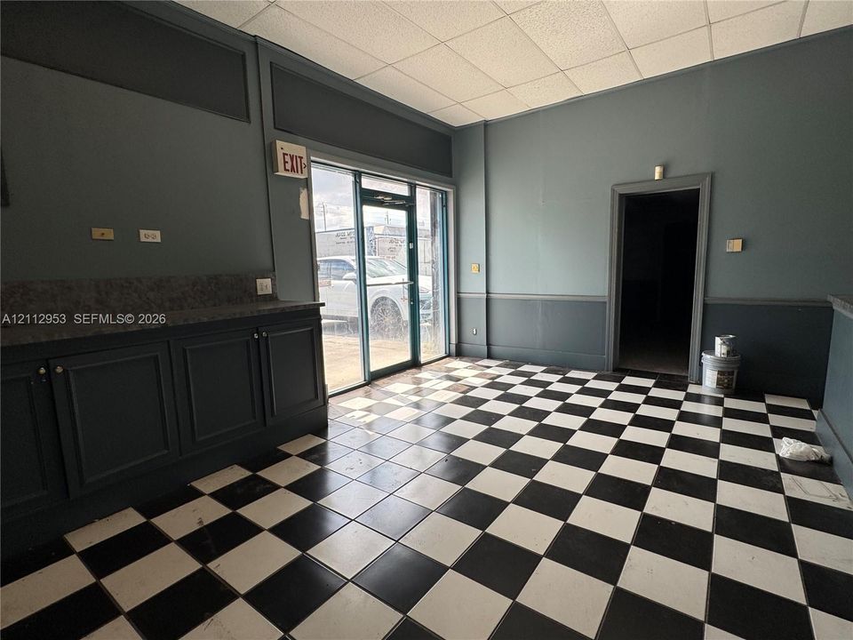Interior space featuring a checkered tile floor, built-in cabinetry with stone-finish countertops, glass-paned entry door, and acoustic drop ceiling