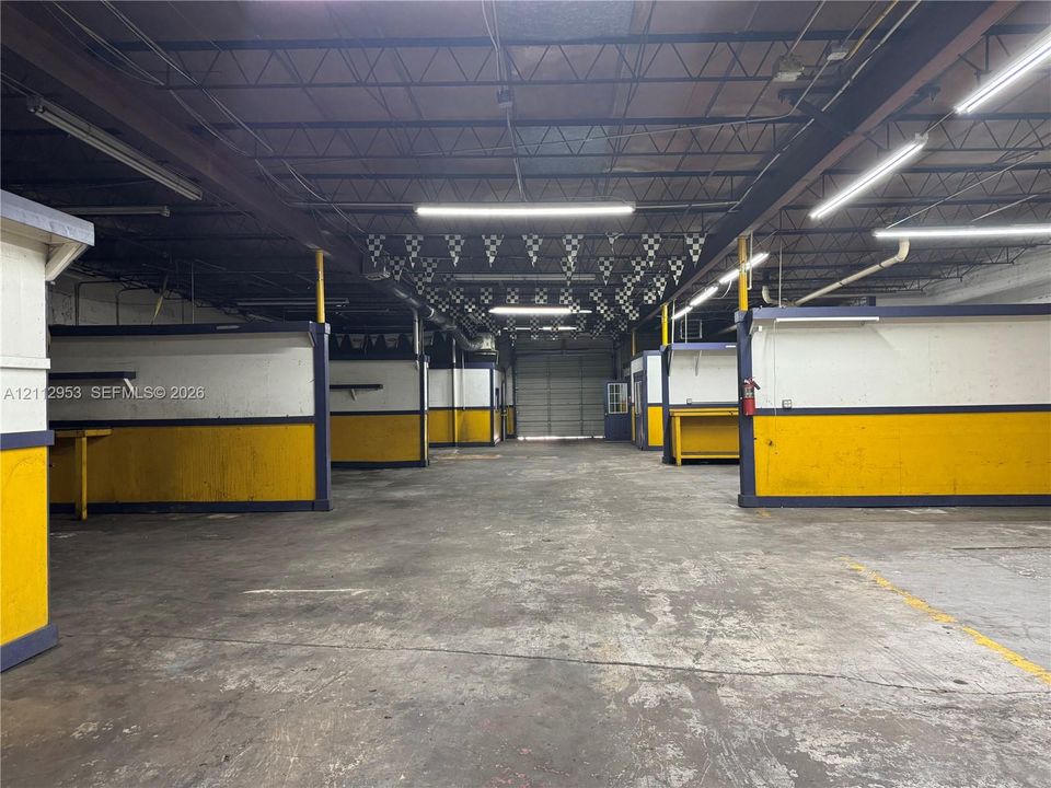 Industrial space featuring an expansive open floor plan, concrete flooring, high-clearance exposed ceiling, LED linear lighting, and roll-up loading door