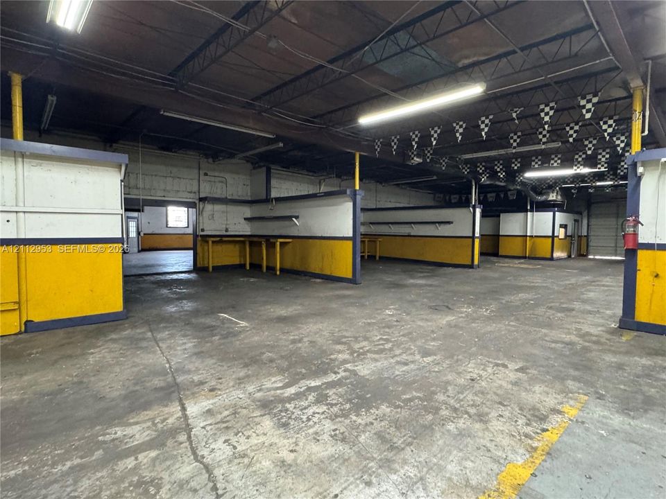 Open-concept commercial space featuring concrete flooring, exposed ceiling beams, built-in wall shelving, and industrial overhead lighting