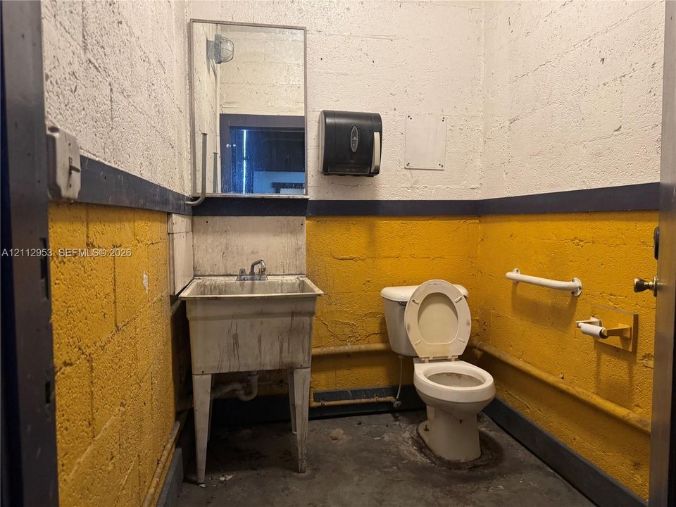 Restroom featuring painted concrete block walls, a pedestal-style utility sink, a wall-mounted paper towel dispenser, and a white grab bar