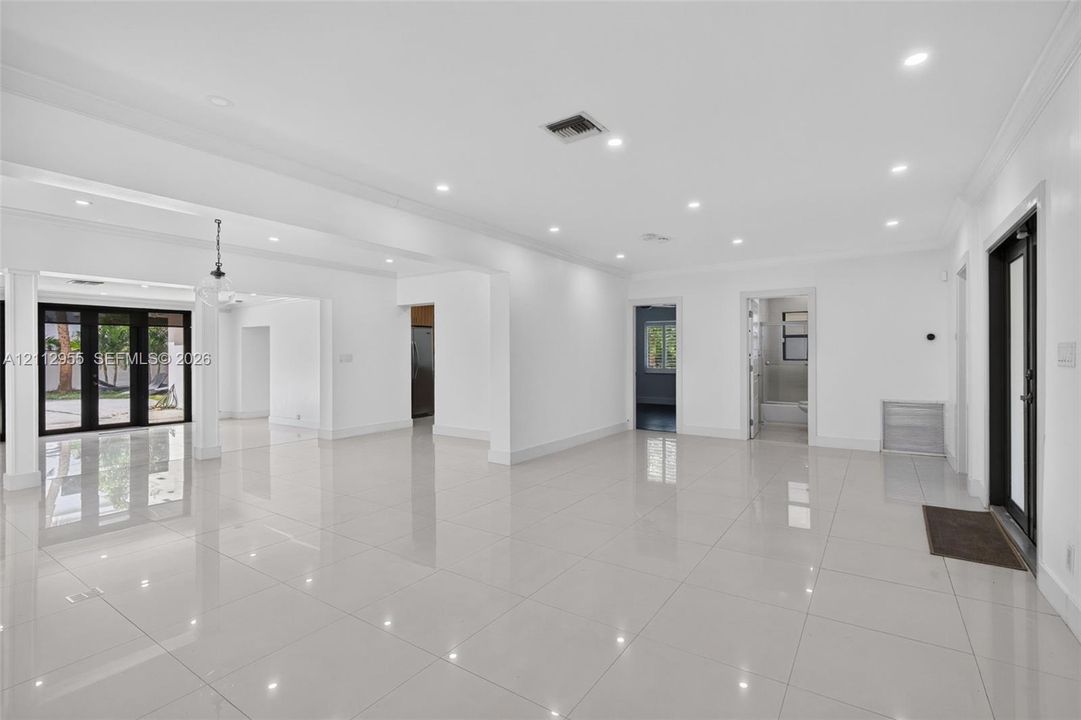 Open-concept interior featuring large-format tile flooring, recessed ceiling lighting, crown molding, and black-framed glass patio doors