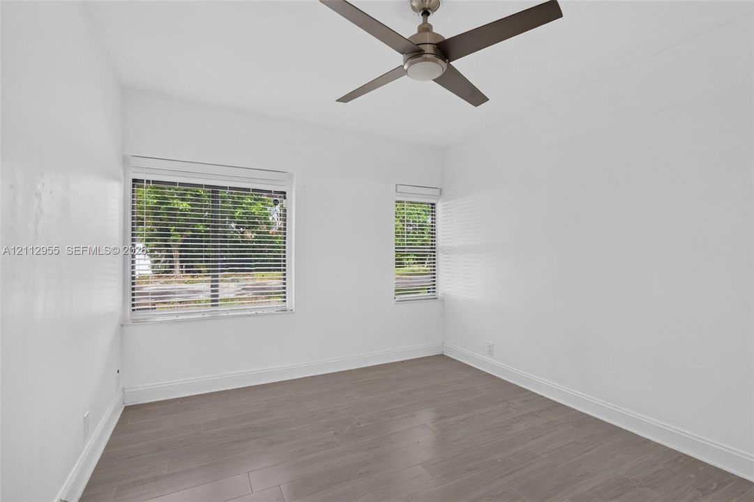 Room featuring wood-finish flooring, a matte-finish ceiling fan, and horizontal window blinds