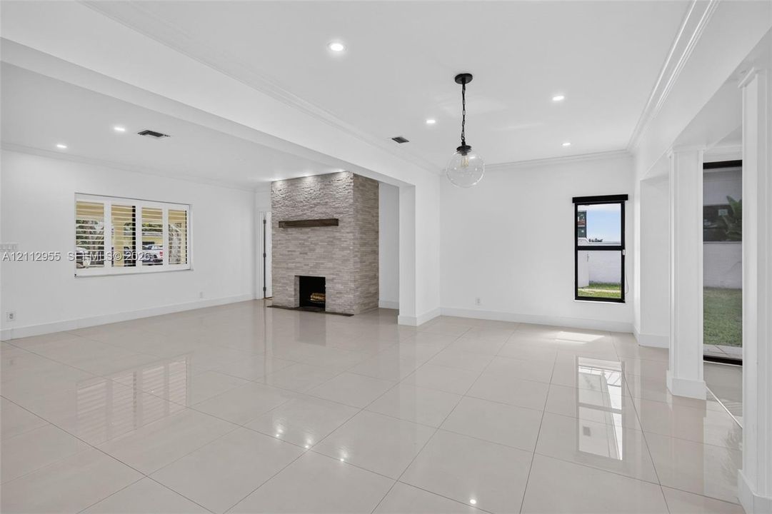 Open-concept interior featuring light-toned tile flooring, a floor-to-ceiling stacked stone fireplace with a wood mantel, recessed lighting, and a modern glass pendant fixture