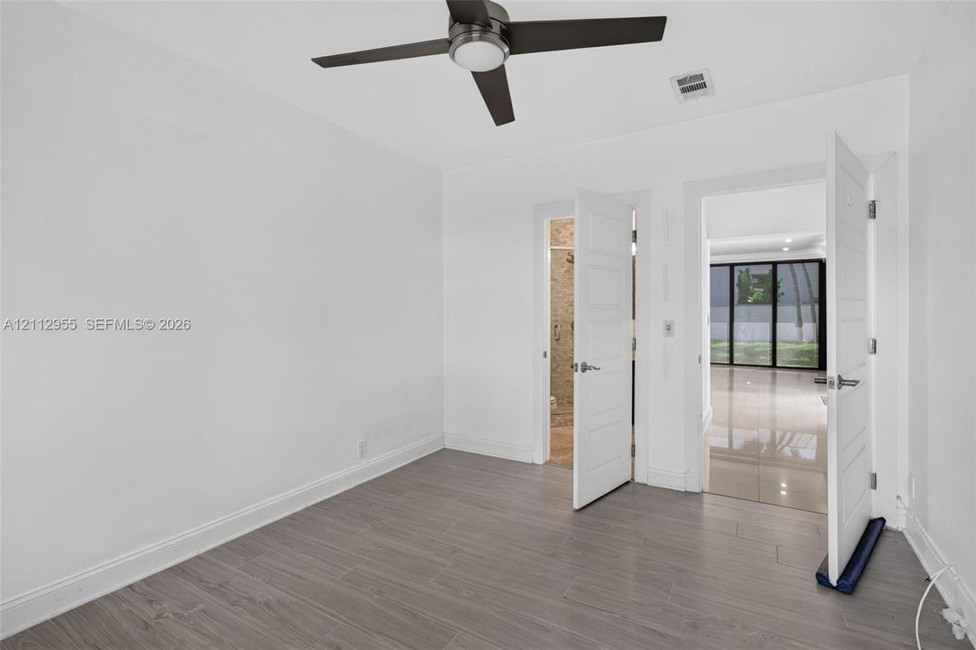 Neutral-toned wood-finish flooring, ceiling fan with integrated light, and solid-core interior doors