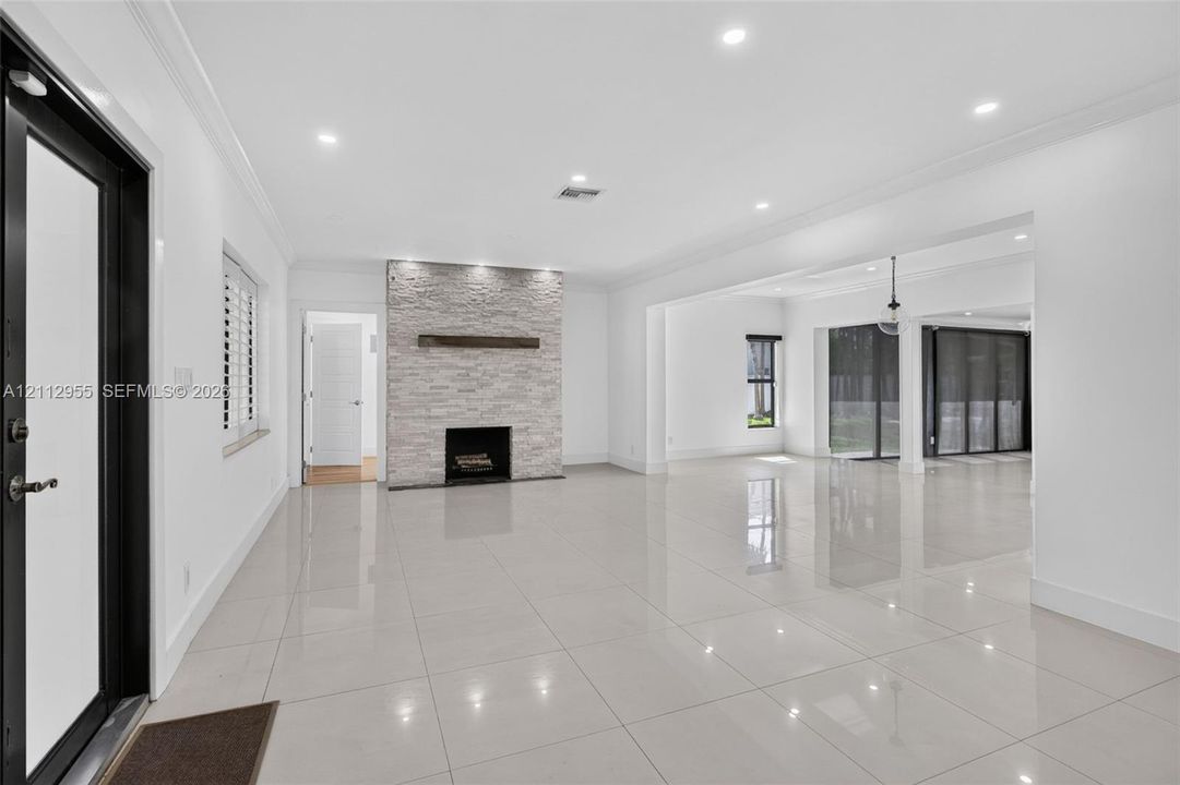 Open-concept interior featuring large-format polished tile flooring, stone-veneer fireplace with a wood mantel, recessed ceiling lighting, and floor-to-ceiling glass sliding doors