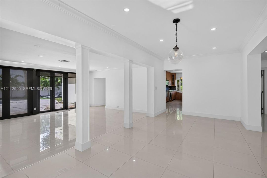 Open-concept interior featuring large-format polished tile flooring, recessed lighting, architectural columns, and dark-framed glass paneled doors