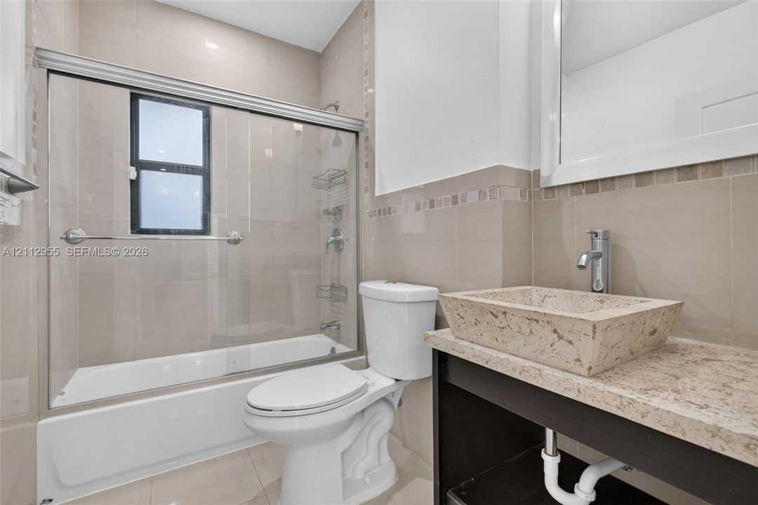 Bathroom featuring a custom stone vessel sink with a chrome faucet, solid-surface vanity countertop, glass-enclosed shower with tiled walls, and decorative accent tiling