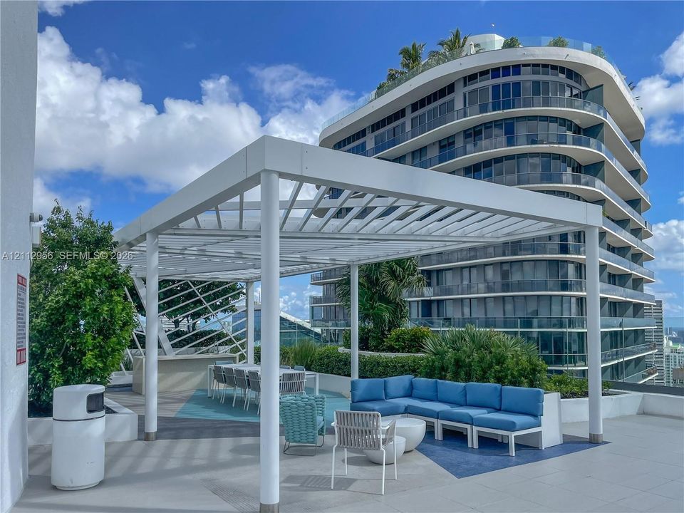 Outdoor terrace featuring a white pergola, built-in bar, tiered landscaping, and paved flooring
