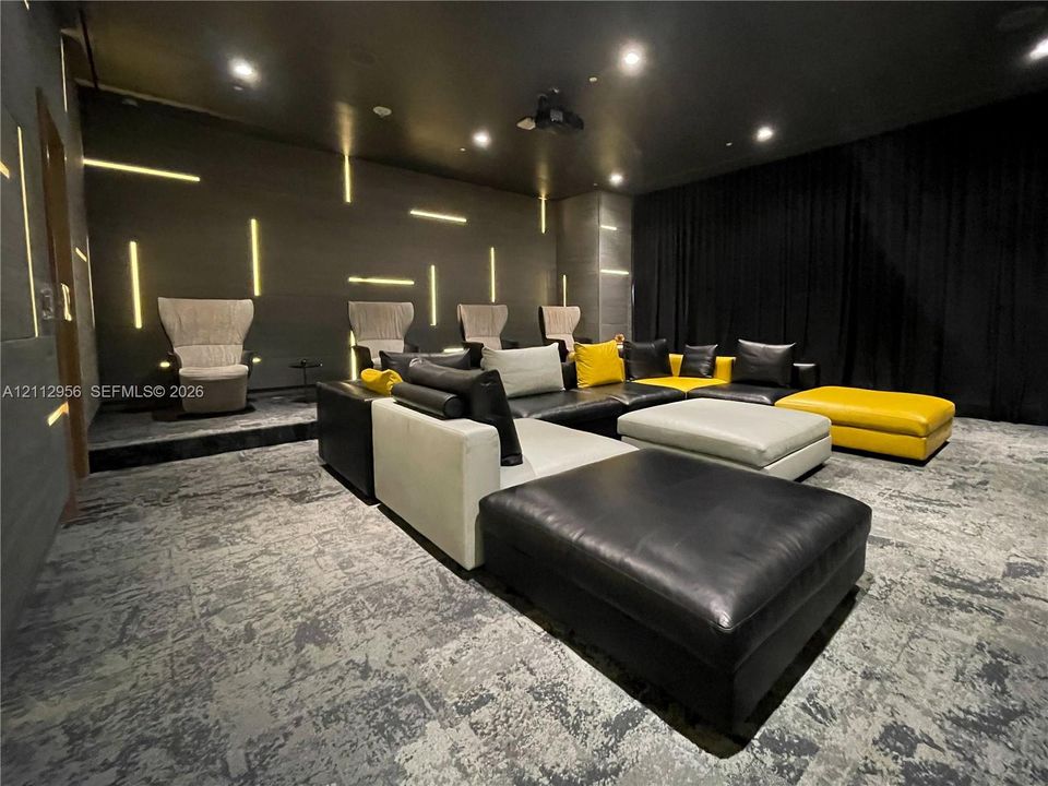 Dedicated media room featuring tiered seating platforms, integrated linear wall lighting, recessed ceiling lighting, and stone-textured wall paneling
