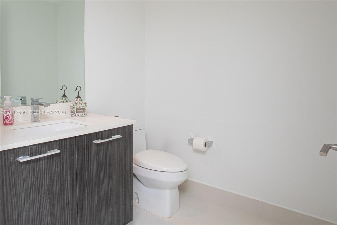 Bathroom featuring a dark wood-finish vanity, white countertop, integrated rectangular sink, single-lever chrome faucet, and wall-mounted mirror