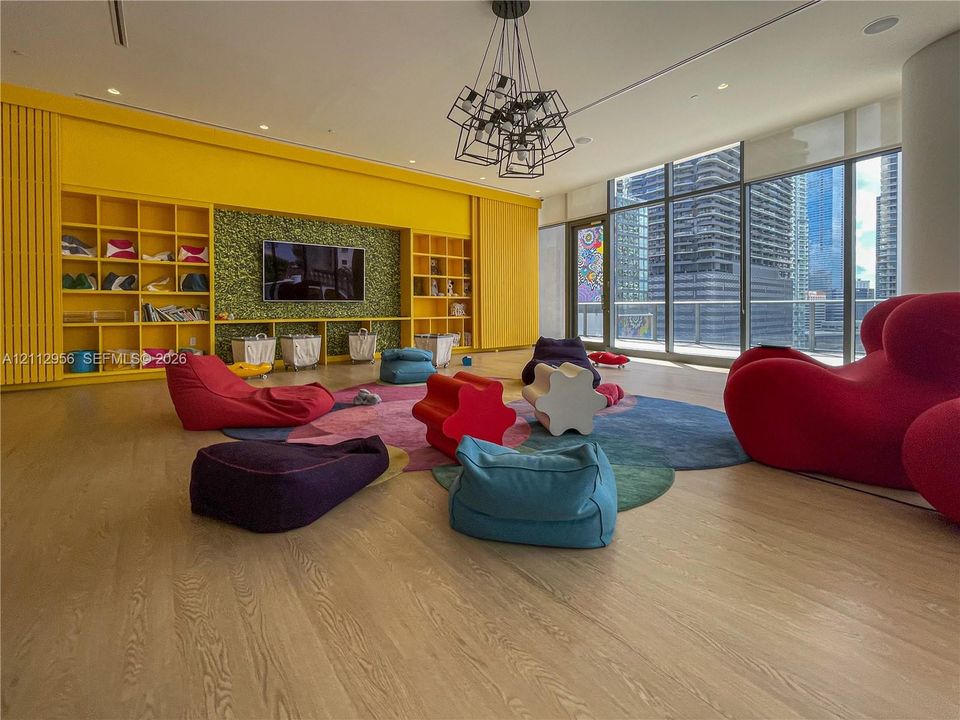 Floor-to-ceiling windows, built-in shelving with integrated textured wall paneling, wood-finish flooring, and a modern geometric chandelier
