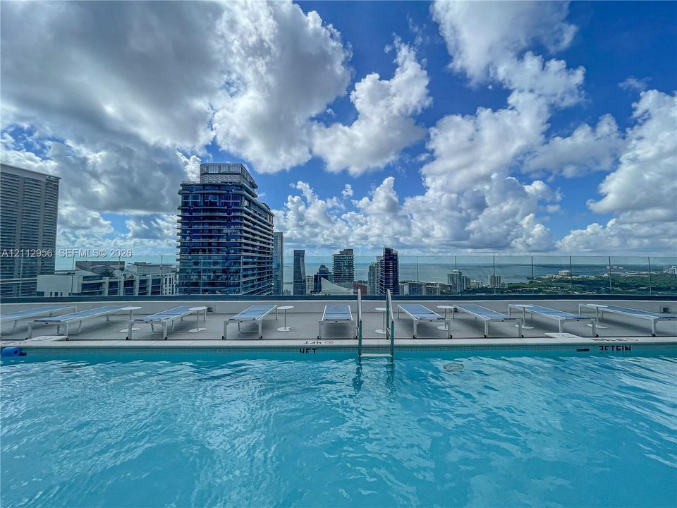 Rooftop swimming pool featuring a glass balustrade and stone-surfaced deck with built-in metal pool ladder
