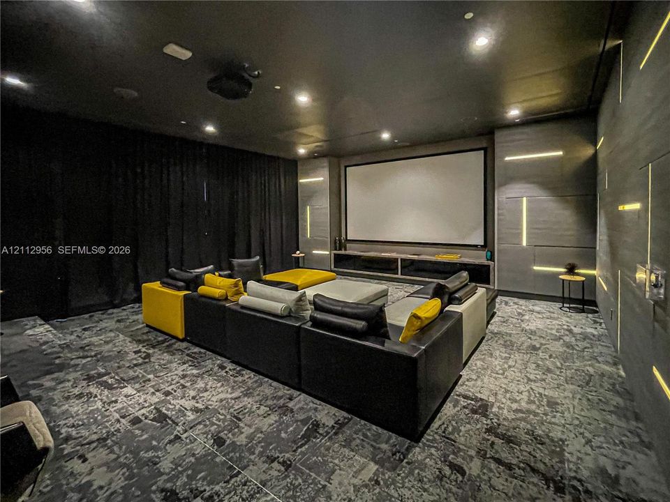 Media room featuring a recessed projection screen, built-in media console, integrated LED wall lighting, ceiling-mounted downlights, and textured wall paneling