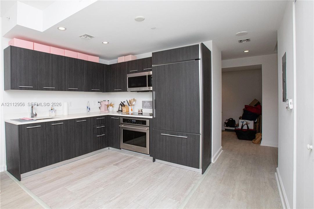 Kitchen featuring dark wood-finish cabinetry, light-toned stone countertops, built-in stainless steel appliances, recessed ceiling lighting, and light wood-finish flooring