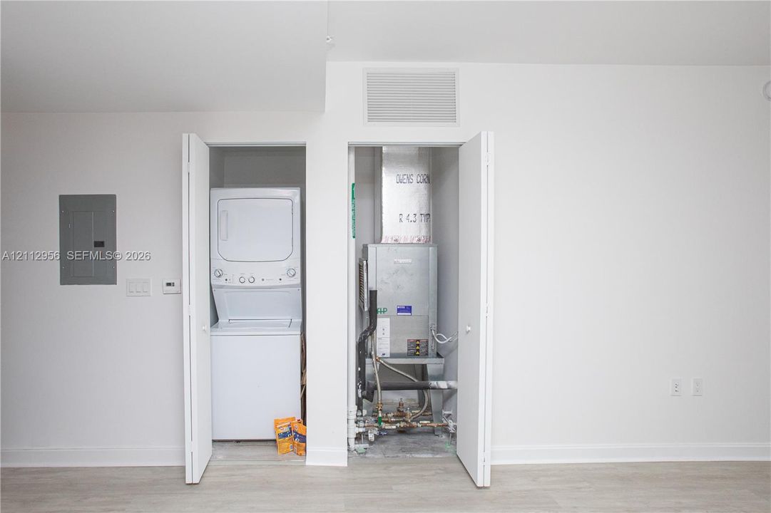 Laundry closet equipped with a stacked washer and dryer, adjacent utility closet housing mechanical systems, and electrical panel