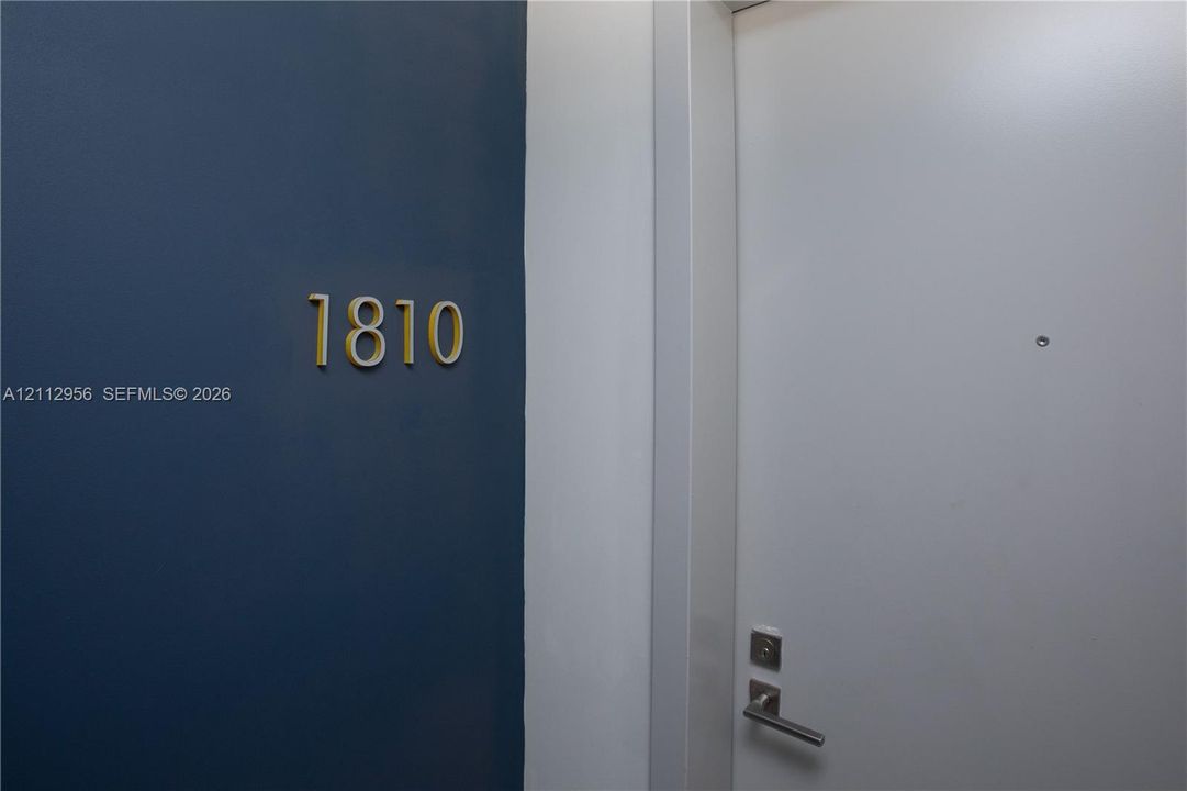 Entry door featuring a metallic security peephole, lever-style handle, and dedicated brass-tone numerals set against a contrast-color wall