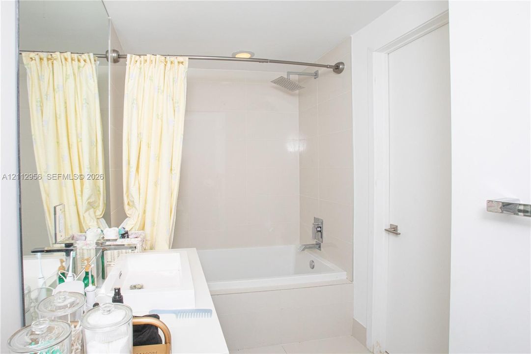 Full-wall vanity mirror, white rectangular vessel sink, solid-surface countertop, tub-shower combination with light-toned wall tile, and wall-mounted rain shower head
