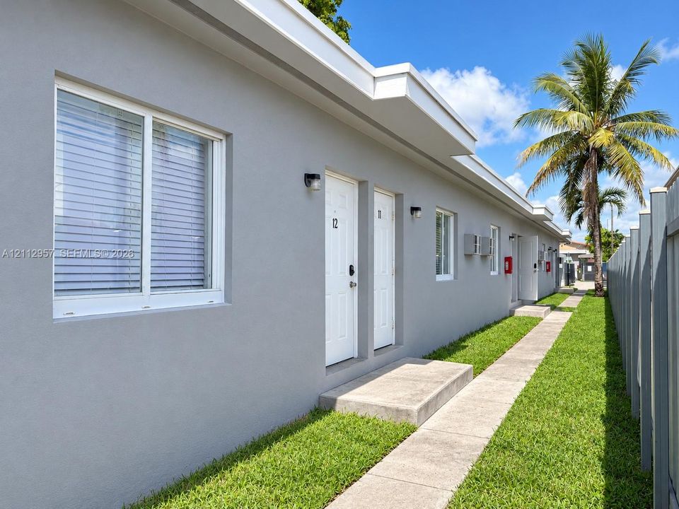 Stucco exterior featuring dual-pane sliding windows, concrete entry steps, wall-mounted exterior lighting, and a paved walkway bordered by manicured lawn