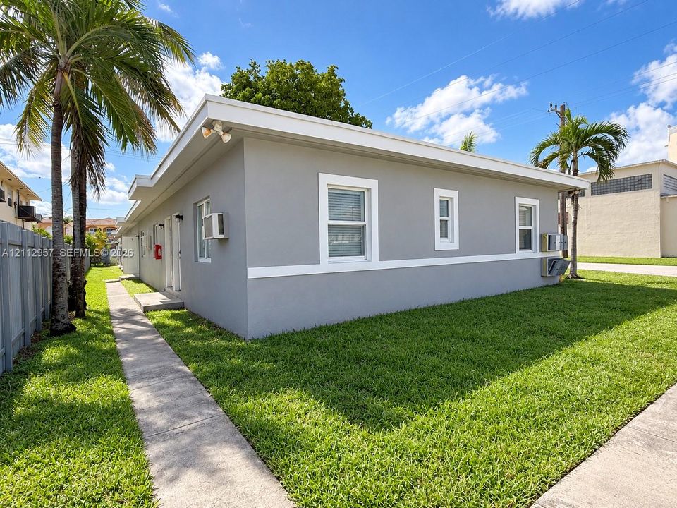 Single-story exterior featuring a neutral grey stucco facade, white trim detailing, flat roofline, and concrete walkway