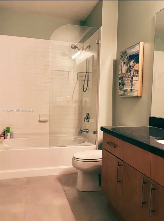 Bathroom featuring a vanity with dark stone-finish countertop, wood-finish cabinetry, a glass shower enclosure, and a wall-to-wall mirror