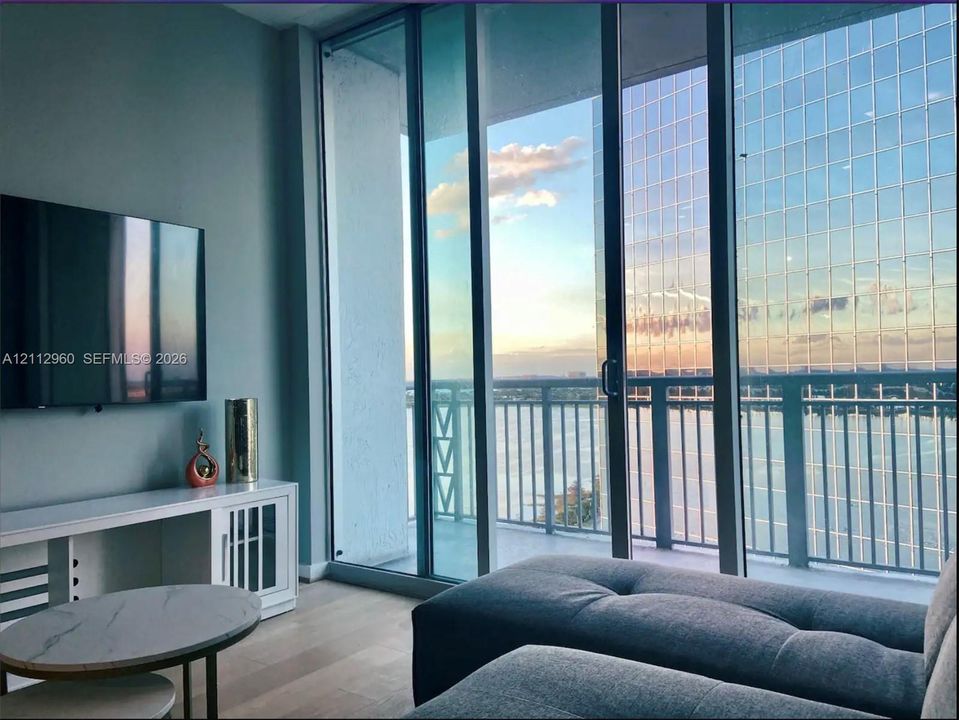 Floor-to-ceiling glass sliding doors, private balcony with metal railing, and wood-finish flooring