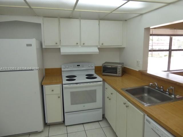 Kitchen featuring white cabinetry, wood-tone countertops, stainless steel sink, and white appliances including an electric range and refrigerator