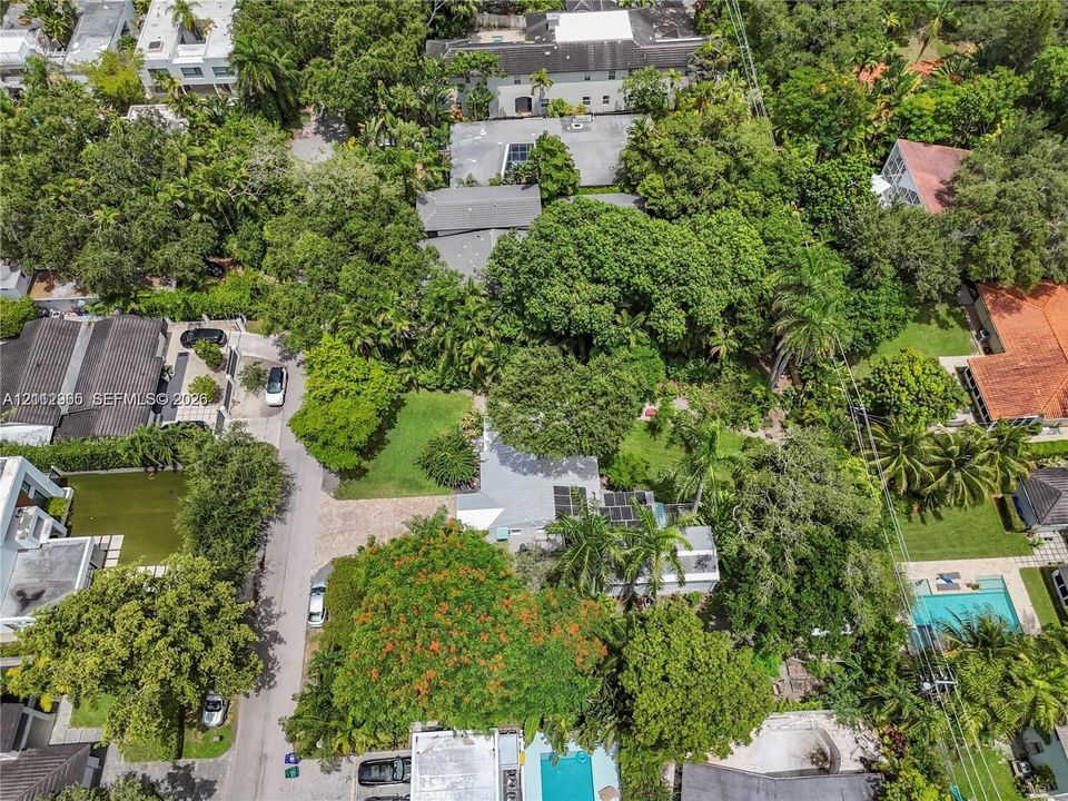 Aerial perspective of a property featuring mature tree canopy, expansive lawn space, and hardscaped driveway area