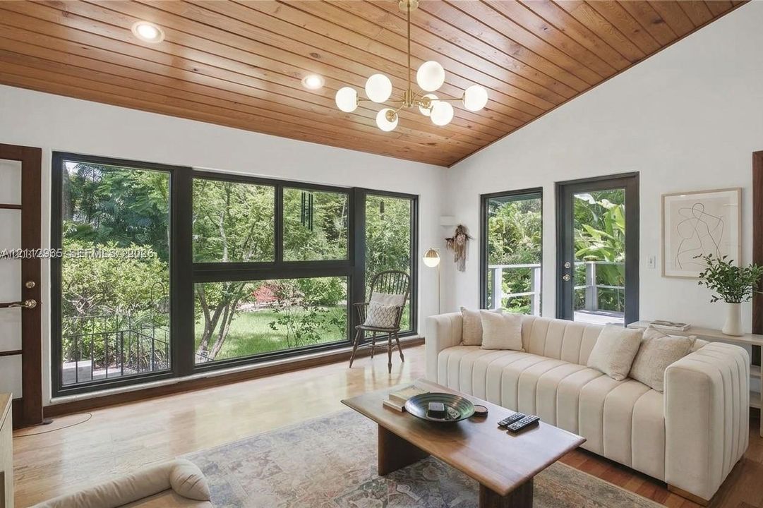 Vaulted wood-plank ceiling featuring a multi-light globe chandelier, expansive floor-to-ceiling windows with black framing, and light-toned wood-finish flooring