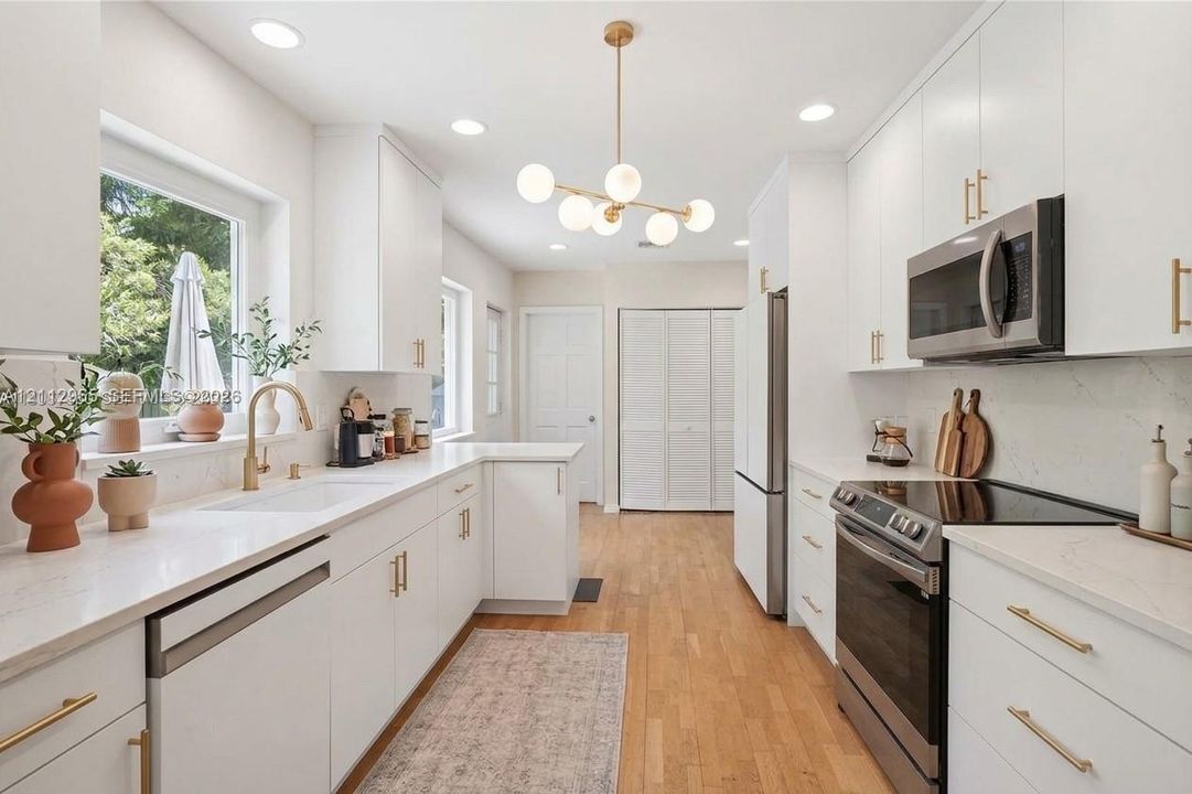 Kitchen featuring white cabinetry with gold-toned hardware, solid-surface countertops, wood-finish flooring, stainless steel appliances, and a modern multi-globe chandelier