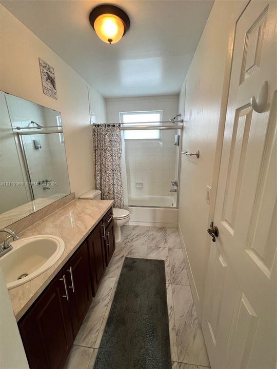 Full bathroom featuring a single-sink vanity with a solid-surface countertop, dark-finish cabinetry, tile flooring, and a combined tub and shower enclosure with tile surround