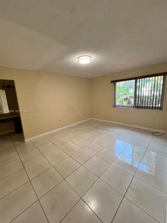 Spacious room featuring neutral tile flooring, a flush-mount ceiling light fixture, and a large window with vertical blinds