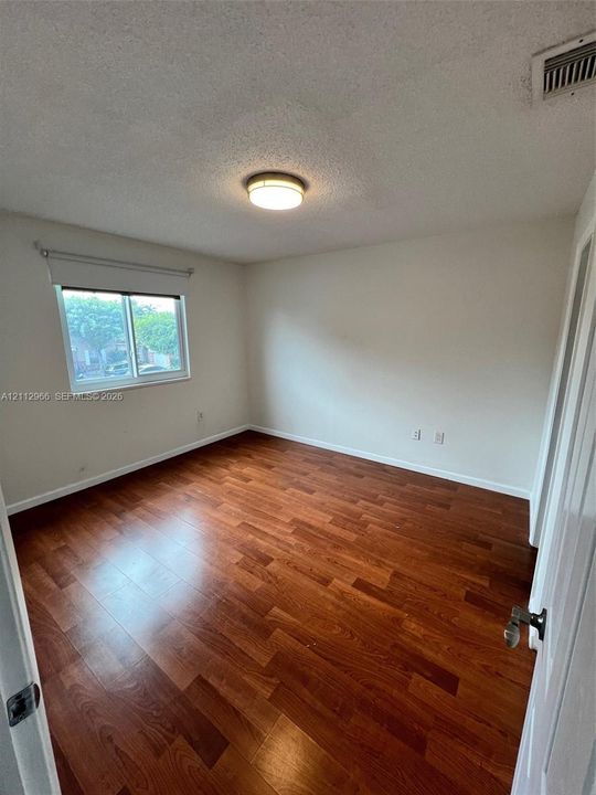 Room featuring wood-finish flooring, neutral wall paint, and a central flush-mount ceiling light fixture