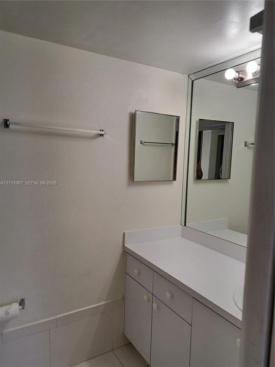 Bathroom vanity featuring solid surface countertop, white cabinetry with integrated storage, wall-to-wall vanity mirror, and mounted light fixture