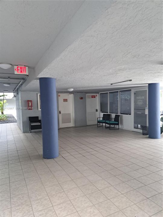 Covered outdoor common area featuring tile flooring, structural pillars, flush-mount ceiling lighting, and aluminum-framed glazing