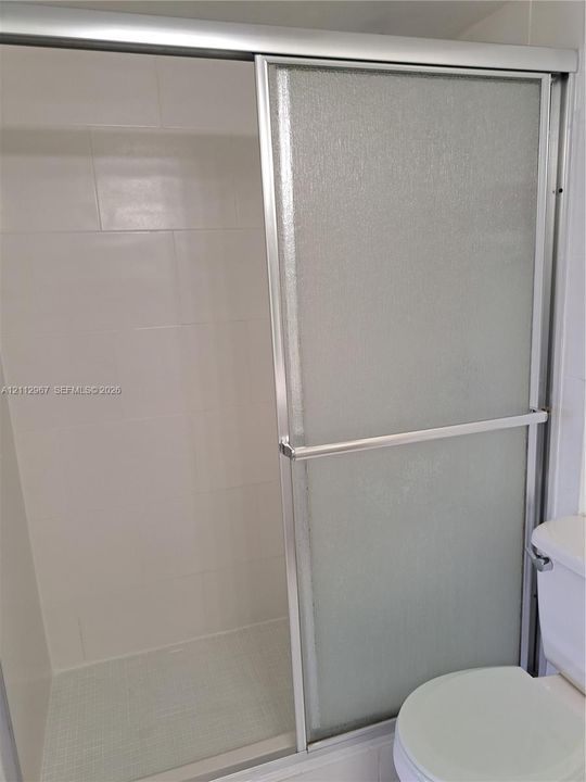 Walk-in shower enclosure featuring sliding frosted glass doors, silver-toned metal framing, and tiled interior walls