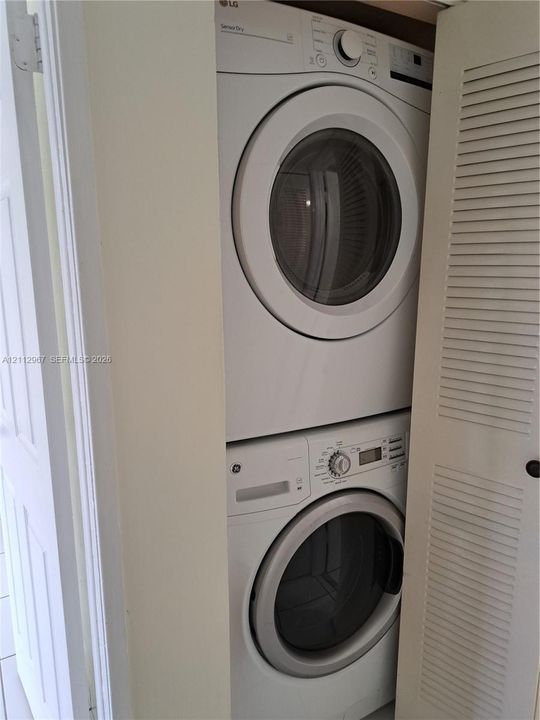 Stacked white washer and dryer unit enclosed within a louvered-door closet