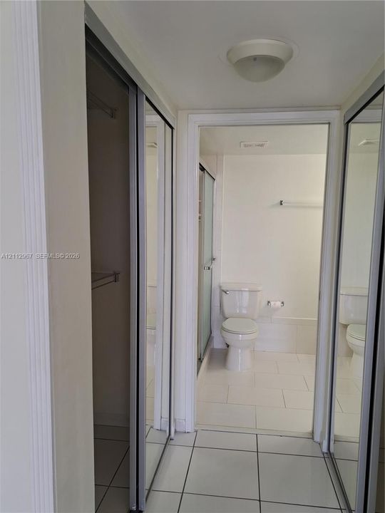 Dual mirrored sliding-door closet featuring integrated shelving and hanging rods, tiled flooring, and a flush-mount ceiling light fixture