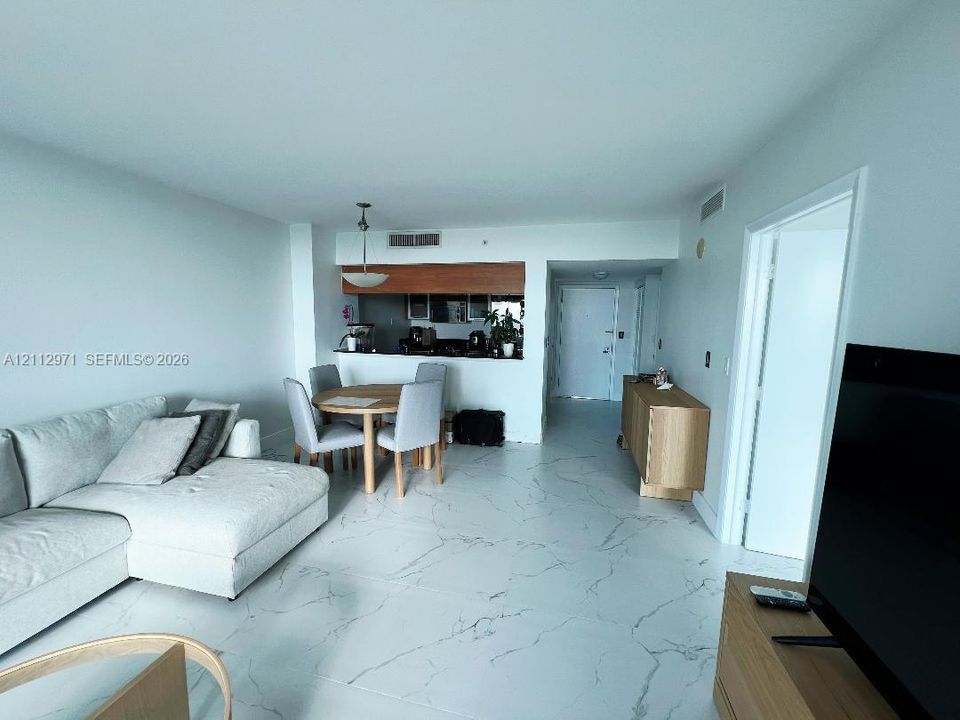 Large-format tile flooring with veining detail, kitchen featuring stone-surfaced breakfast bar, and a hanging pendant light fixture